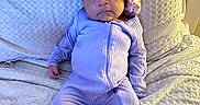 Emanii is registered to the contest to win money with this photo: baby, infant, child, portrait, lying_down, blanket, bed, lavender, onesie, bonnet, floral, clothing, face, eyes, serious_expression, indoor, cozy, textile, photography, cute