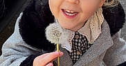 Lou a rejoint le concours — aidez-le/la à gagner de superbes lots ! toddler, child, girl, smiling, dandelion, outdoor, coat, gray_coat, fur_trim, blue_eyes, hair_buns, holding, happy, cute, street, footwear, person, young_child, playful, closeup