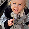 toddler, child, girl, smiling, dandelion, outdoor, coat, gray_coat, fur_trim, blue_eyes, hair_buns, holding, happy, cute, street, footwear, person, young_child, playful, closeup