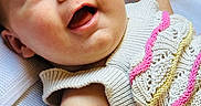 Ember is registered to the contest to win money with this photo: baby, blue_eyes, child, closeup, colorful, cute, face, happy, indoors, infant, knitted_clothing, lying_down, newborn, pink, portrait, skin, smiling, soft_texture, white, yellow