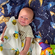 Bentley is registered to the contest to win money with this photo: baby, blanket, bee_pattern, blue_blanket, stars, moon, toys, plush_toy, lion_toy, frog_toy, pacifier, crib, mesh, infant, smiling, clothing, indoor, cute, child, playing