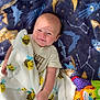 baby, blanket, bee_pattern, blue_blanket, stars, moon, toys, plush_toy, lion_toy, frog_toy, pacifier, crib, mesh, infant, smiling, clothing, indoor, cute, child, playing
