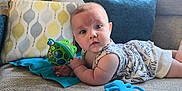 Aria is registered to the contest to win money with this photo: baby, infant, toy, frog_toy, couch, pillow, blanket, clothing, face, person, child, indoor, curious, blue, white, patterned, soft_lighting, cute, laying_down, closeup