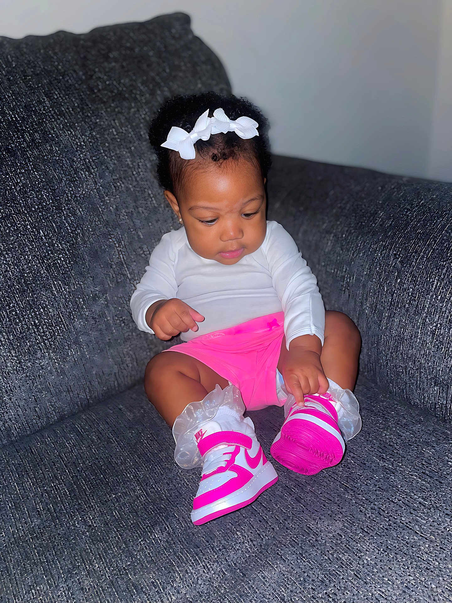 Tia is registered to the contest to win money with this photo: toddler, child, sneakers, pink, white, bow, headband, socks, couch, grey, clothing, footwear, indoor, person, cute, baby, sitting, focused, fashion, portrait