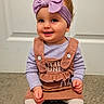 baby, child, smiling, headband, bow, outfit, brown, lavender, carpet, door, indoor, cute, happy, sitting, person, toddler, long_sleeve, white_buttons, clothing, portrait
