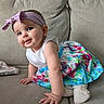 baby, child, girl, headband, dress, colorful, floral, couch, sofa, living_room, smile, cute, curious, indoors, person, infant, sitting, hand, footwear, apparel