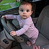 baby, child, car, steering_wheel, seat, hand, clothing, onesie, indoors, person, wide_eyes, looking_at_camera, foot, tattoo, dashboard, window, greenery, background, curious, cute