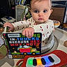 baby, child, book, dinosaurs, trucks, onesie, high_chair, toy_piano, lights, indoor, face, eyes, hands, furniture, living_room, reading, expression, cute, person, playtime