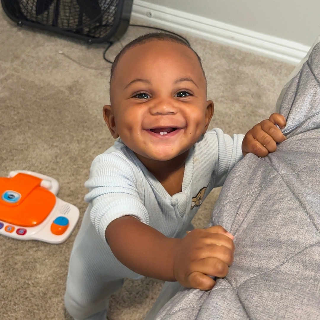 Toriyan joined the competition — help win amazing prizes! baby, bedspread, carpet, child, clothing, cute, dimples, face, fan, fingers, hand, happy, home, indoors, infant, person, play, smiling, standing, toy