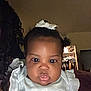 Railey is registered to the contest to win money with this photo: baby, child, face, indoor, portrait, white_bow, clothing, curly_hair, glossy_lips, gaze, person, soft_lighting, hand, fingernail_art, closet, furniture, dark_skin, young_child, cute, closeup
