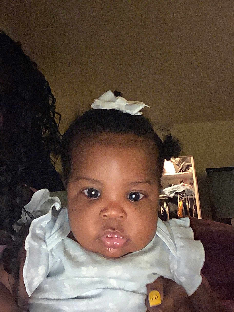 Railey is registered to the contest to win money with this photo: baby, child, face, indoor, portrait, white_bow, clothing, curly_hair, glossy_lips, gaze, person, soft_lighting, hand, fingernail_art, closet, furniture, dark_skin, young_child, cute, closeup