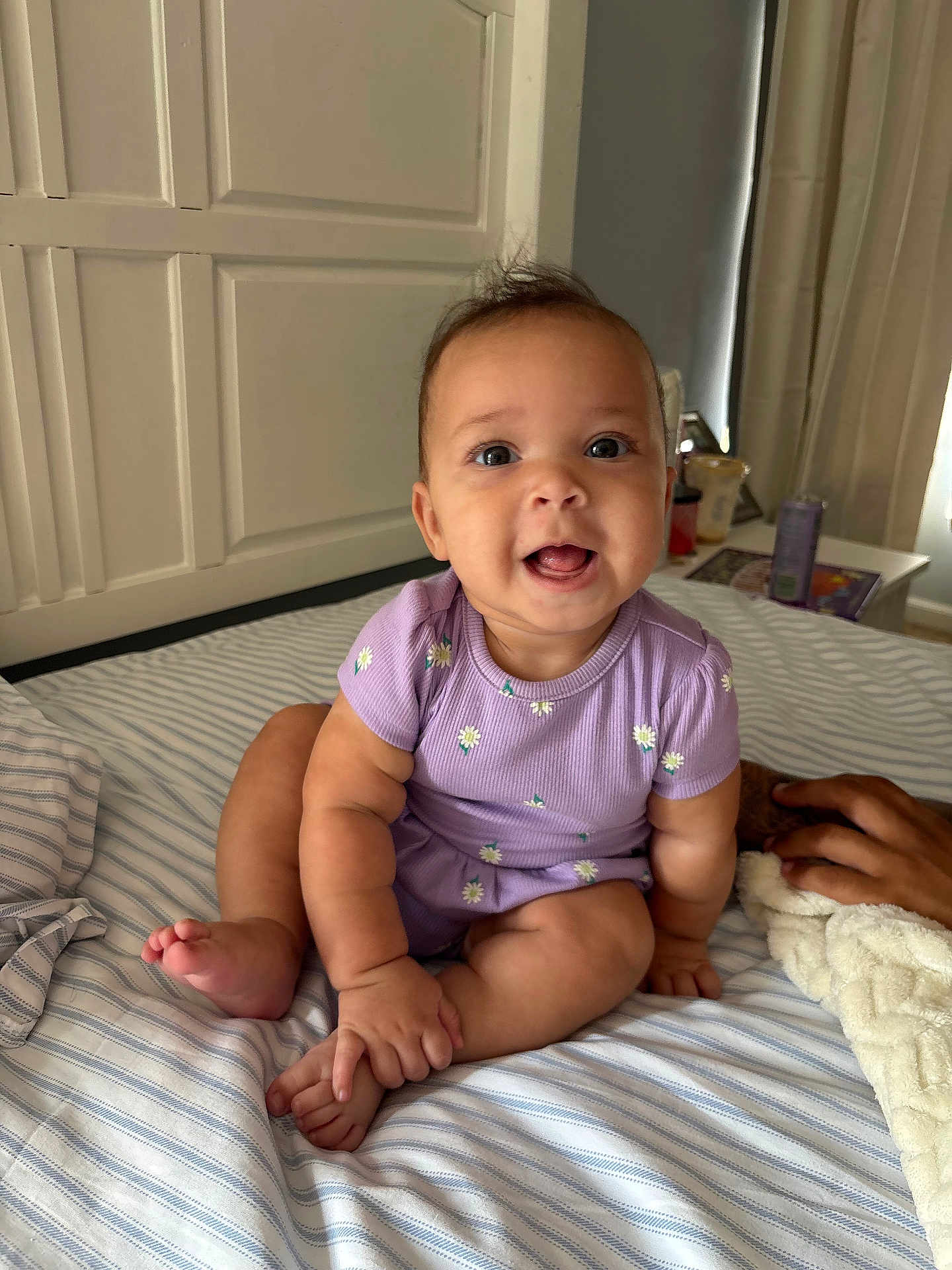 Reighlynn joined the competition — help win amazing prizes! baby, infant, child, purple_clothing, onesie, smiling, happy, sitting, bed, striped_bedspread, hand, blanket, indoor, face, cute, person, room, curtains, furniture, cozy
