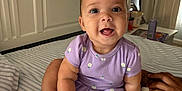 Reighlynn joined the competition — help win amazing prizes! baby, infant, child, purple_clothing, onesie, smiling, happy, sitting, bed, striped_bedspread, hand, blanket, indoor, face, cute, person, room, curtains, furniture, cozy