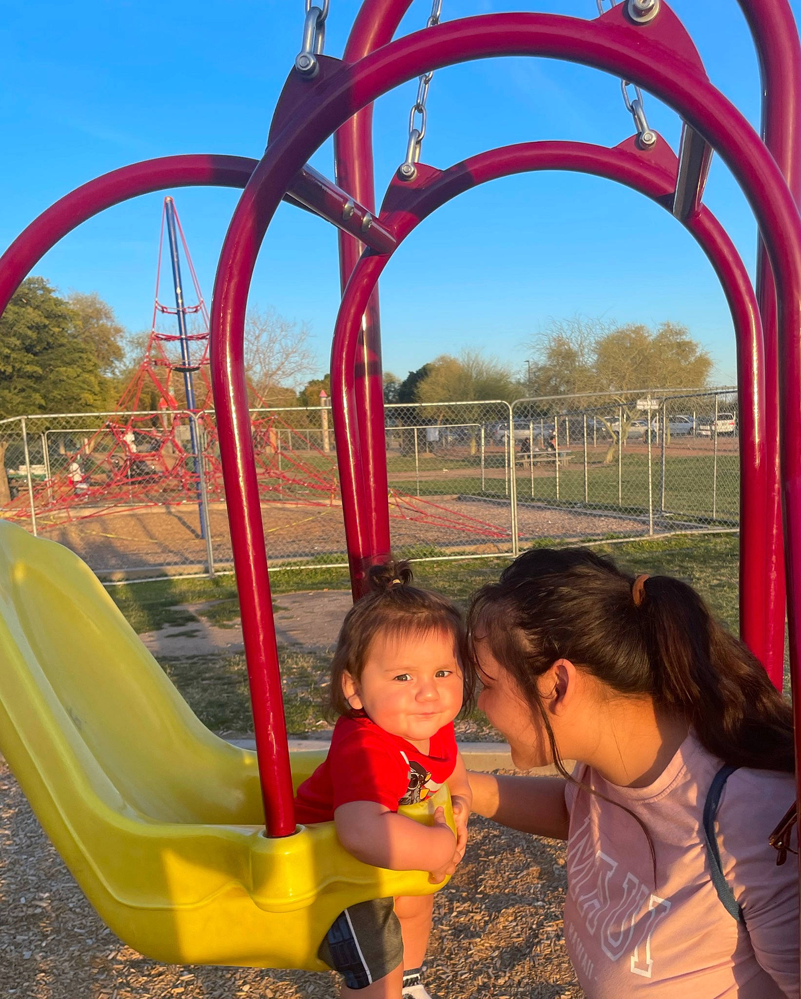 Andres is registered to the contest to win money with this photo: city, clothing, fun, grass, leaf, leisure, nature, outdoor_play_equipment, person, photograph, plant, playground, public_space, recreation, red, sky, summer, toddler, tree, woody_plant