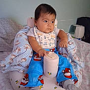 Noe Adan joined the competition — help win amazing prizes! baby, baby_seat, bedroom, bib, blanket, bottle, child, cozy, cup, curious, cushion, furniture, gray_socks, indoor, infant, looking_away, pajamas, portrait, santa_pattern, sitting
