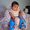 baby, baby_seat, bedroom, bib, blanket, bottle, child, cozy, cup, curious, cushion, furniture, gray_socks, indoor, infant, looking_away, pajamas, portrait, santa_pattern, sitting