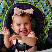 Azareé joined the competition — help win amazing prizes! baby, baby_seat, blue_eyes, bow, cheerful, child, cute, happy, headband, high_chair, indoor, infant, patterned_background, person, pink_shirt, playful, sitting, smiling, tongue_out, waving_hands