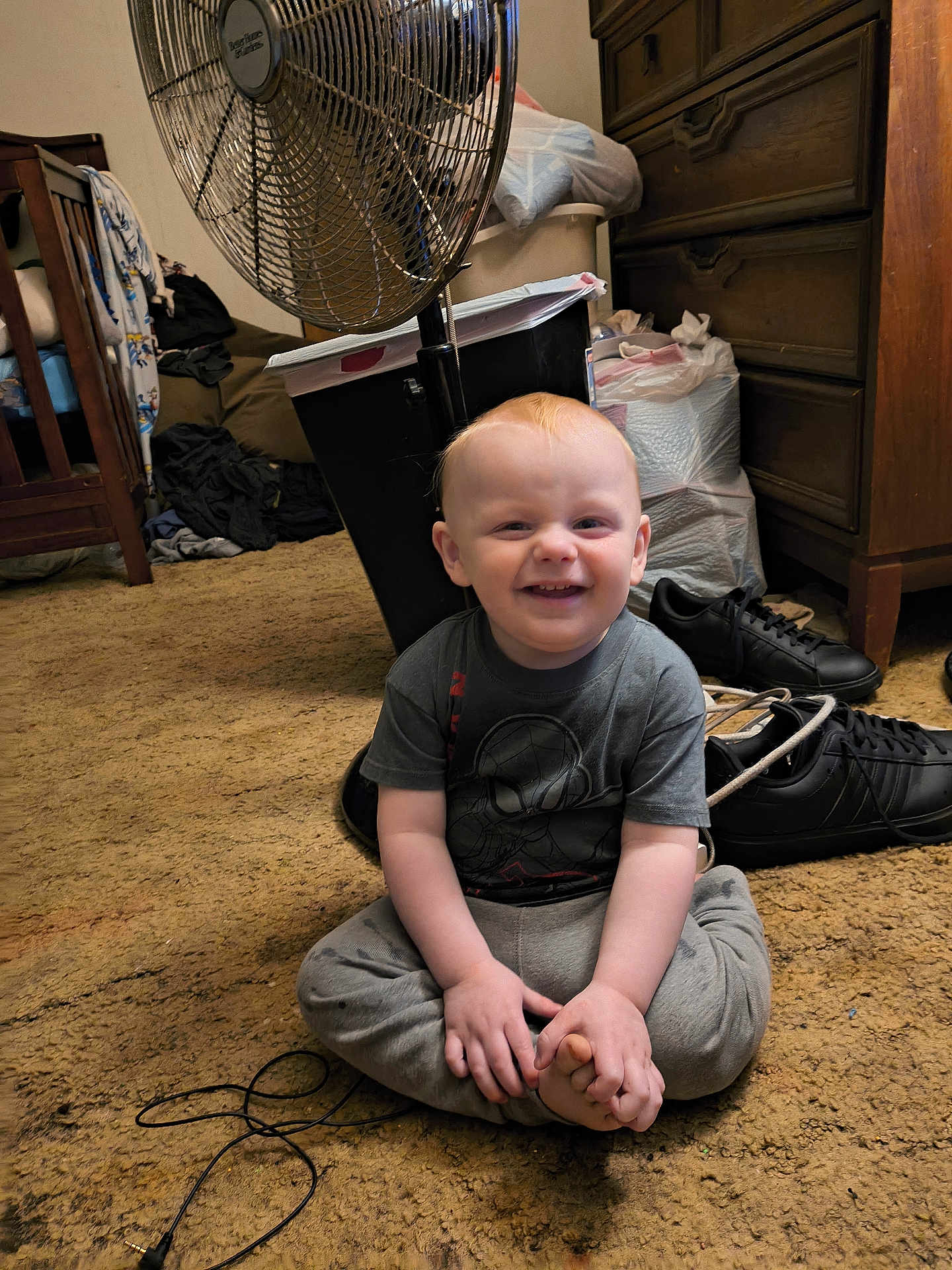 Hardin is registered to the contest to win money with this photo: toddler, child, smiling, sitting, carpet, fan, shoes, dresser, clothing, room, floor, cord, toy, hair, hand, foot, indoor, person, furniture, casual
