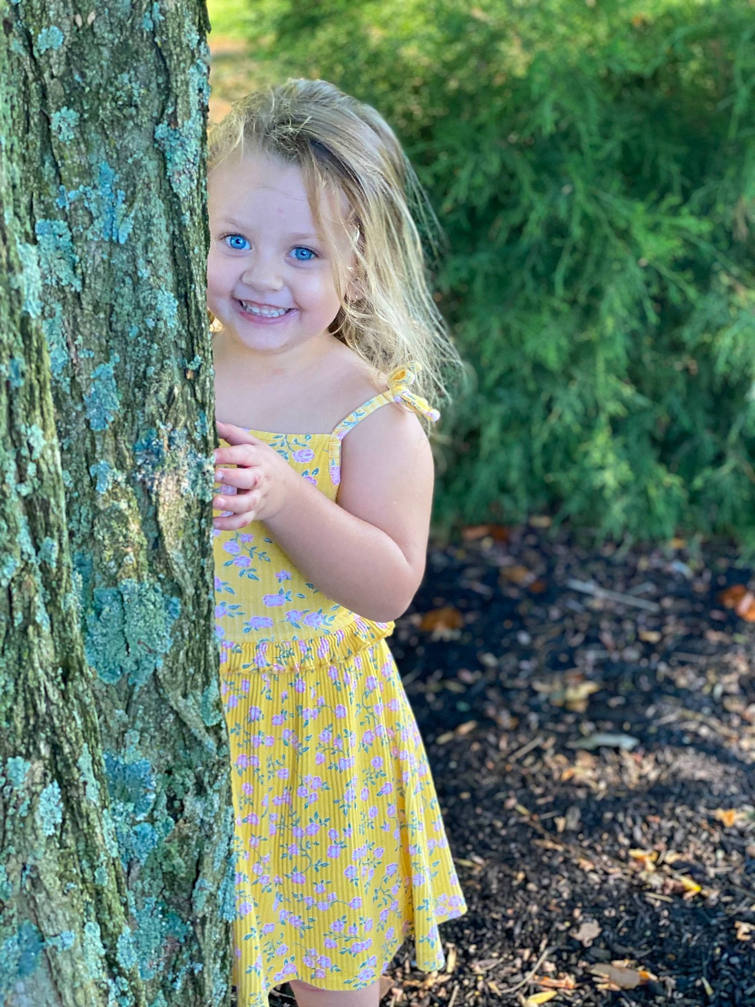 Lydia is registered to the contest to win money with this photo: blond, branch, day_dress, eye, flash_photography, forest, grass, hair, happy, human_body, joy, long_hair, one_piece_garment, people_in_nature, person, plant, smile, toddler, tree, trunk