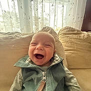 Silas joined the competition — help win amazing prizes! baby, child, clothing, couch, cozy, curtain, face, happy, home, indoor, infant, natural_light, pillow, portrait, seated, sleeves, smiling, vest, window, zipper