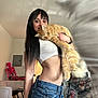 black_hair, casual, cat, couch, denim_shorts, exercise_bike, furniture, holding, indoor, living_room, long_hair, orange_cat, pet, portrait, relaxed, skeleton_decoration, smile, table, white_top, woman