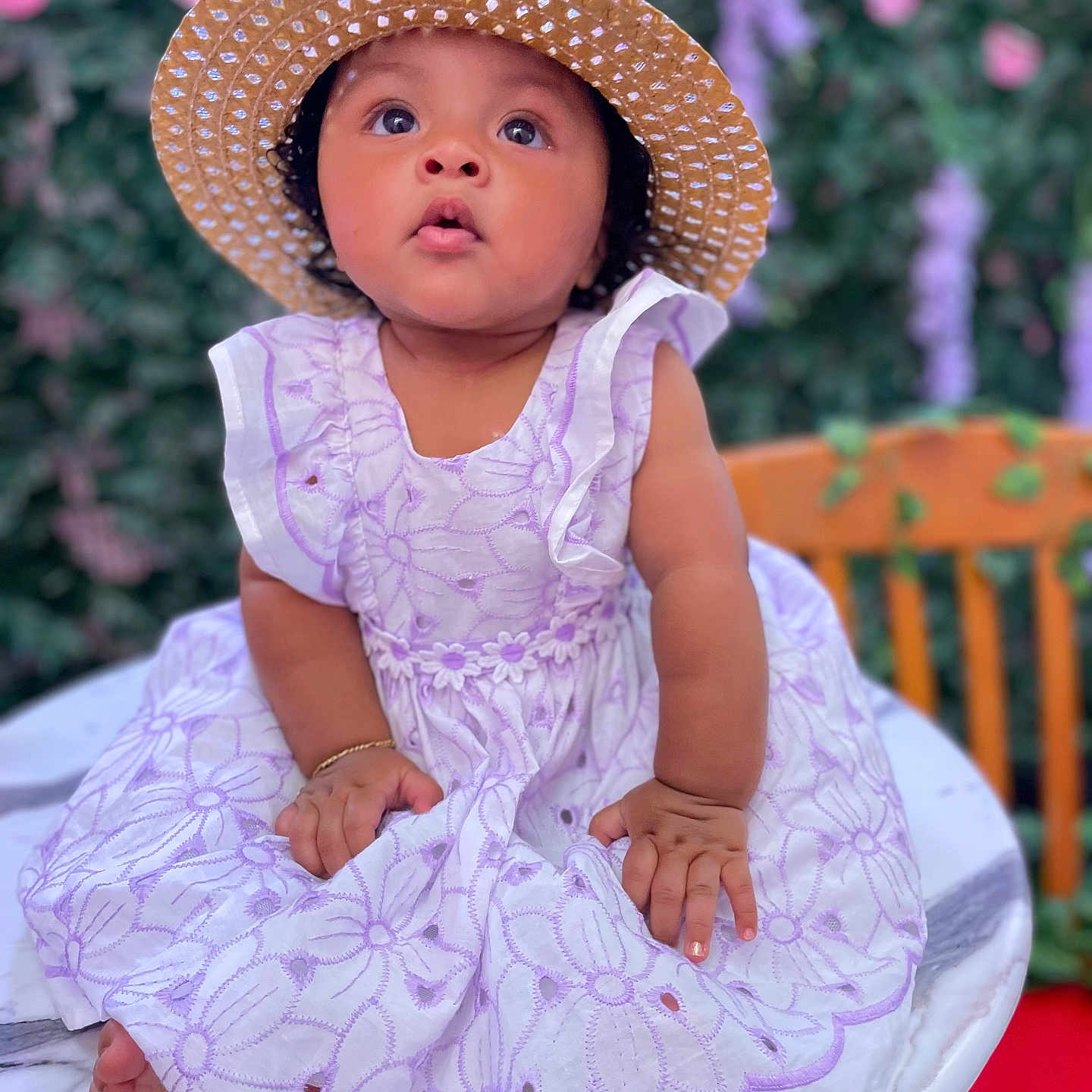Kilany is registered to the contest to win money with this photo: baby, background, child, cute, dress, expression, floral_pattern, flowers, girl, greenery, hands, hat, marble_table, outdoor, portrait, sitting, skin, straw_hat, table, wide_eyes
