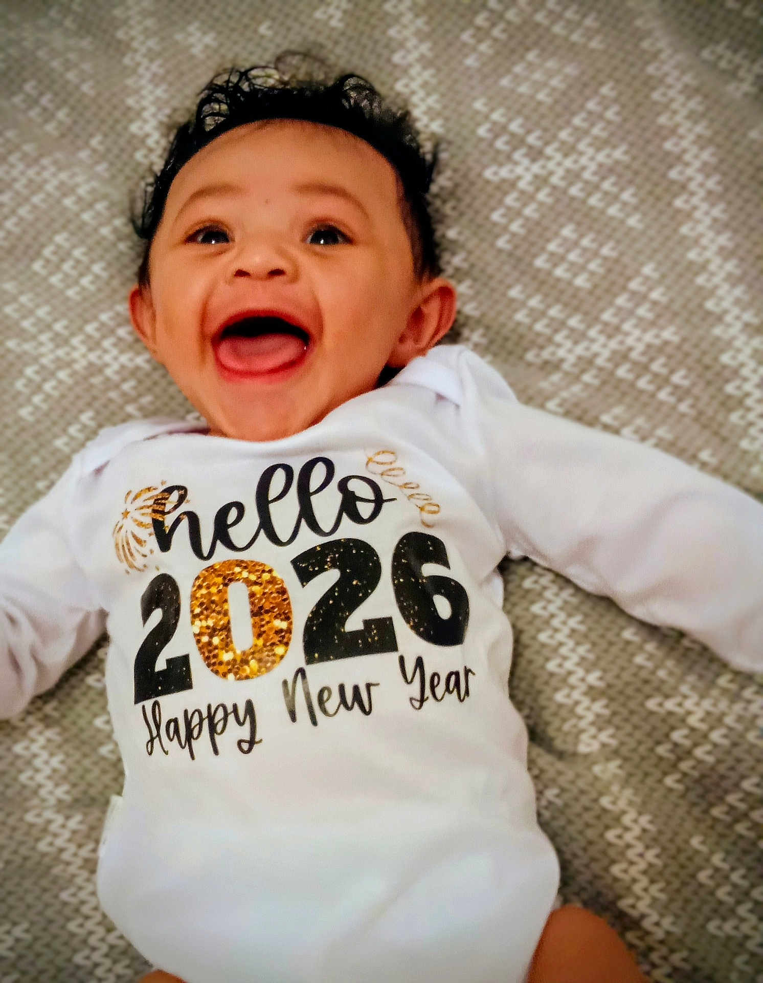 élior participe au concours pour gagner de l'argent avec cette photo : baby, infant, child, smiling, laughing, onesie, text_on_clothing, new_year, 2026, happy, lying_down, blanket, pattern, face, open_mouth, eyes, hair, cute, portrait, celebration