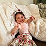 baby, child, smile, happy, couch, blanket, floral, headband, pants, pink, shoes, indoor, cozy, cute, person, infant, clothing, sitting, home, portrait