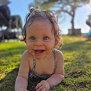 Myla a rejoint le concours — aidez-le/la à gagner de superbes lots ! baby, baby_girl, blue_eyes, child, closeup, clothing, curly_hair, daylight, face, grass, hands, happy, infant, nature, outdoor, playful, portrait, smiling, summer, sunlight