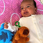 Viyan Reddy is registered to the contest to win money with this photo: baby, infant, child, stuffed_toy, plush_toy, bed, blanket, quilt, clothing, white_outfit, hand, face, head, lying_down, soft_toy, pink_background, cute, expression, indoor, person