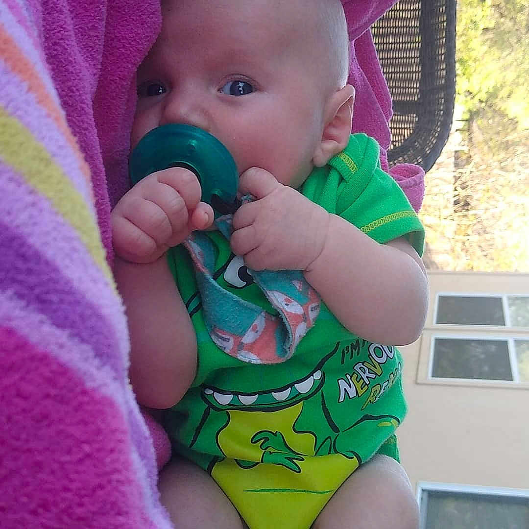 Riley is registered to the contest to win money with this photo: arm, baby, baby_toddler_clothing, cheek, finger, green, hand, happy, head, human_body, mouth, nose, one_piece_swimsuit, organ, photograph, pink, skin, sleeve, swimwear, toddler