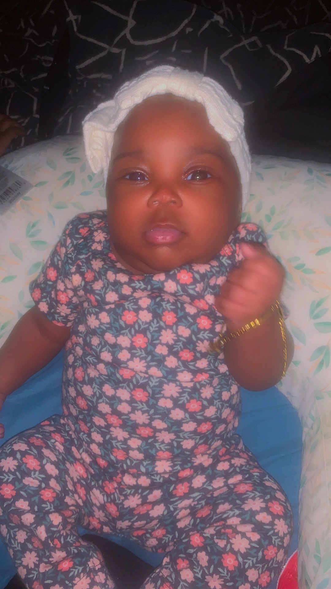 Skylar joined the competition — help win amazing prizes! baby, child, floral_onesie, headband, bracelet, fist, cushion, patterned, indoor, portrait, cute, infant, person, expression, clothing, sitting, closeup, adorable, soft_lighting, home