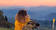 Vana a rejoint le concours — aidez-le/la à gagner de superbes lots ! animal, companionship, curly_hair, dog, evening, grass, hill, landscape, mountains, nature, outdoor, peaceful, person, pet, scenic, sitting, sky, sunset, view, yellow_jacket