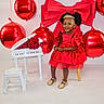 child, girl, red_dress, tiara, balloons, red_balloons, miniature_piano, roses, smiling, sitting, stool, happy, indoor, celebration, dress, gold_shoes, afro_hair, toy, decor, portrait