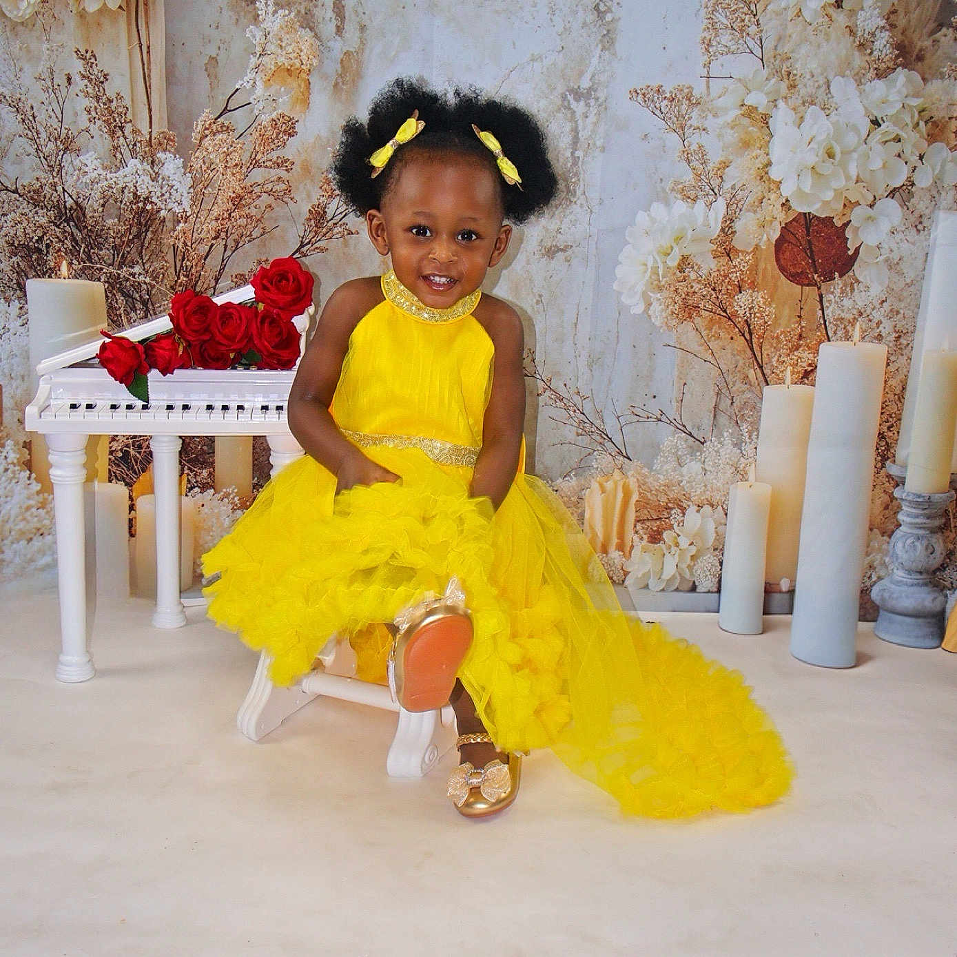 Brihanna Pierre is registered to the contest to win money with this photo: toddler, child, yellow_dress, smiling, afro_hairstyle, bows, golden_shoes, chair, white_piano, red_roses, candles, dried_flowers, studio, portrait, happy, sitting, dress, footwear, background, indoors