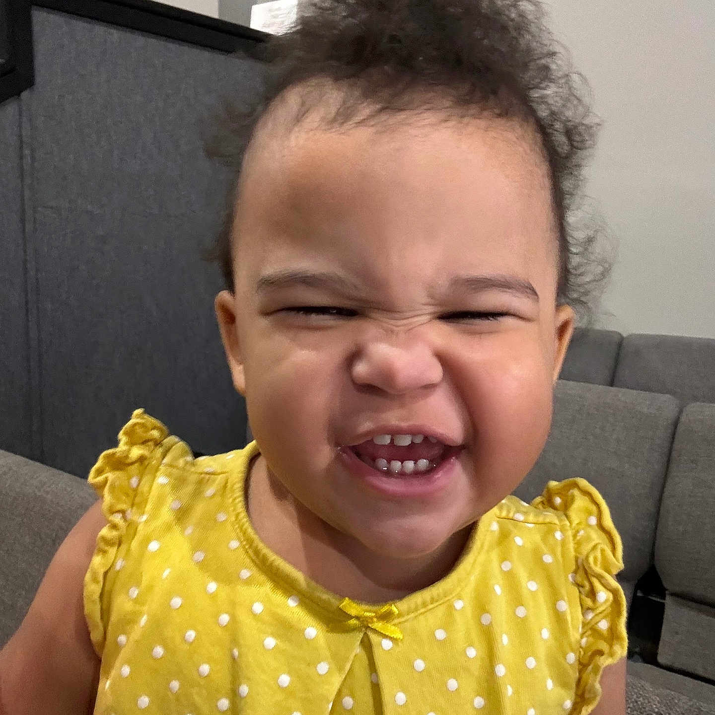 Caylynn is registered to the contest to win money with this photo: baby, child, infant, smiling, laughing, portrait, close_up, face, curly_hair, yellow_dress, polka_dots, ruffles, teeth, happy, indoor, sofa, living_room, seated, candid, joyful