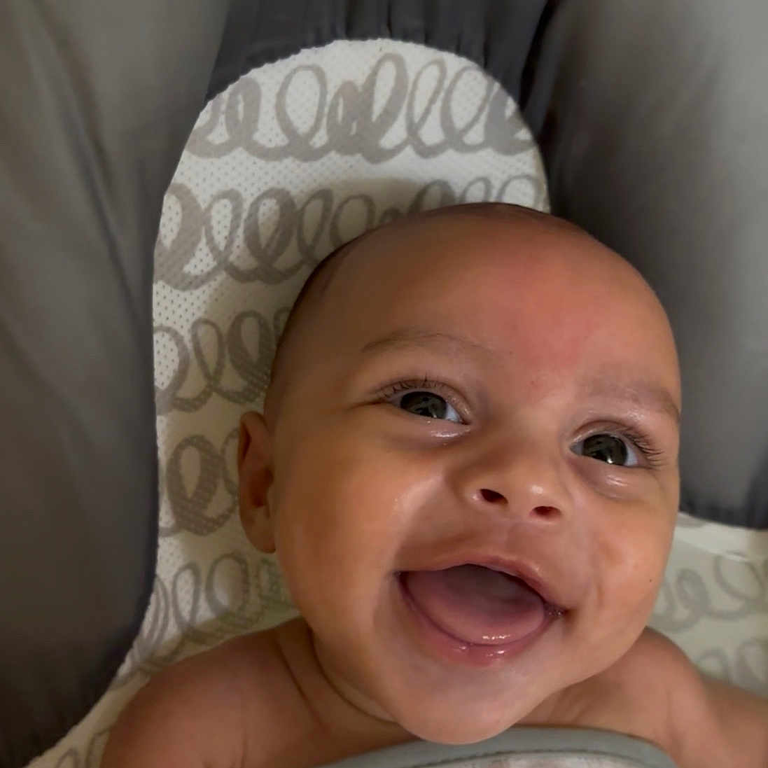 Onzai is registered to the contest to win money with this photo: baby, baby_seat, blanket, child, closeup, cute, expression, face, happy, head, indoors, infant, joyful, lying_down, pattern, person, skin, smiling, wrapped, young_child