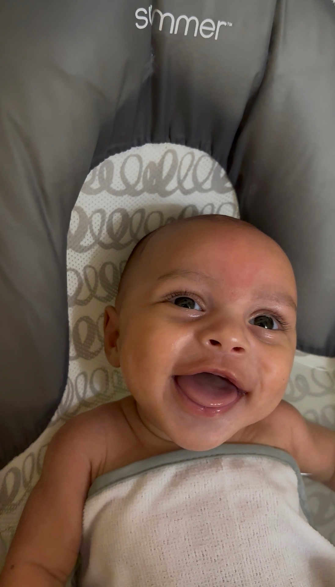 Onzai is registered to the contest to win money with this photo: baby, smiling, infant, blanket, face, happy, lying_down, child, cute, indoors, person, baby_seat, pattern, skin, expression, young_child, joyful, wrapped, closeup, head