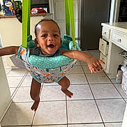 Cayden joined the competition — help win amazing prizes! baby, child, jumper, green_straps, kitchen, tile_floor, smiling, happy, indoor, person, suspended, arms_outstretched, infant, furniture, cabinet, oven, food_packages, doorway, appliance, playtime