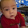 baby, infant, red_sweater, face, eyes, indoors, blanket, table, lights, snowflake_lights, toy, couch, child, expression, curious, warm_lighting, holiday_decor, floor, hand, closeup