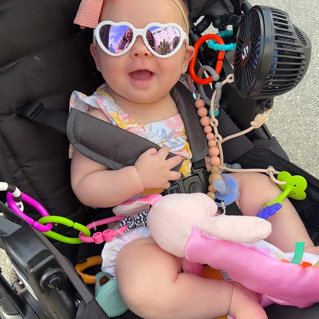 Emma is registered to the contest to win money with this photo: accessories, baby, bodypart, clothing, electronics, face, finger, glasses, goggles, hand, hat, head, person, photography, portrait, strap, stroller, sunglasses, transportation, vehicle