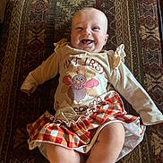 Everleigh is registered to the contest to win money with this photo: baby, smiling, infant, clothing, skirt, patterned_cushion, happy, face, cute, indoor, child, lying_down, cheerful, turkey_design, plaid, legs, feet, long_sleeves, small_child, joyful