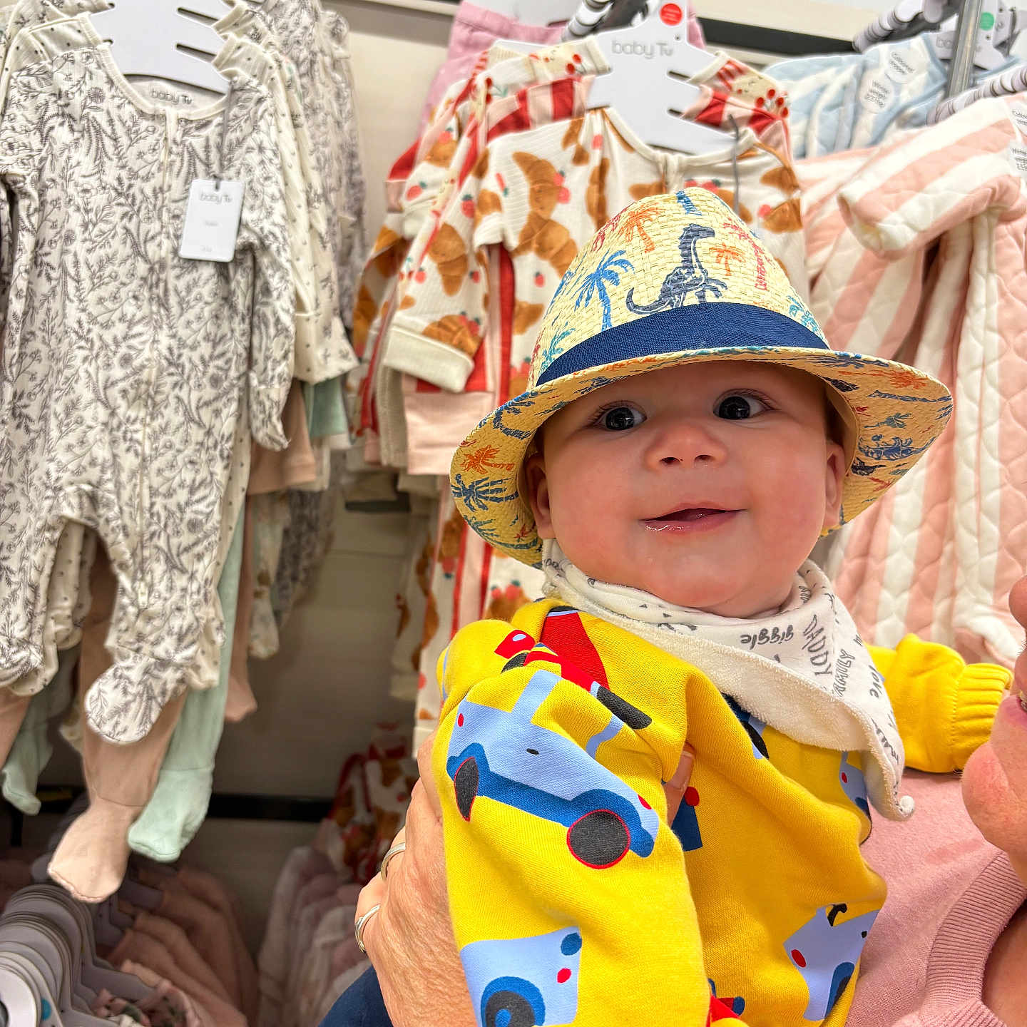 Henry-George is registered to the contest to win money with this photo: adult_hand, baby, baby_clothes, cars_pattern, child, clothing_store, cute, dinosaur_hat, fashion, hanger, happy, hat, indoor, infant, person, portrait, retail, shopping, smiling, yellow_shirt