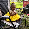 toddler, child, yellow_tutu, bow, outdoor, camping_chair, grass, summer, cute, portrait, baby, sitting, expression, sunlight, nature, playful, casual, clothing, backyard, relaxation