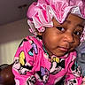 toddler, child, pink_bonnet, pajamas, minnie_mouse, clothing, indoor, portrait, face, curious, person, cute, baby, sleepwear, headwear, sitting, closeup, skin, expression, young_child
