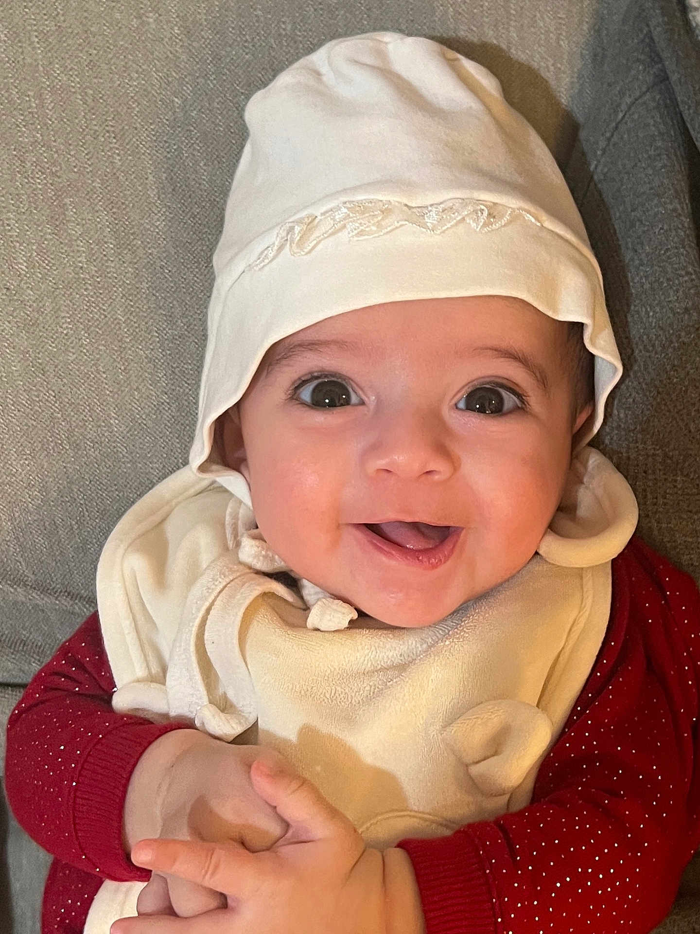 Dhalia joined the competition — help win amazing prizes! baby, infant, child, smile, happy, hat, bonnet, bib, big_eyes, hands, red_sweater, clothing, portrait, closeup, couch, fabric, skin, cheek, mouth, indoor