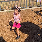 Aryah is registered to the contest to win money with this photo: active, casual, child, fence, fun, girl, happy, headband, jumping, outdoor, person, pink_clothing, play, playground, shadow, smiling, summer, sunlight, trees, wood_chips