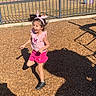 child, girl, playground, jumping, pink_clothing, headband, outdoor, sunlight, shadow, wood_chips, fence, trees, happy, active, casual, summer, play, fun, smiling, person