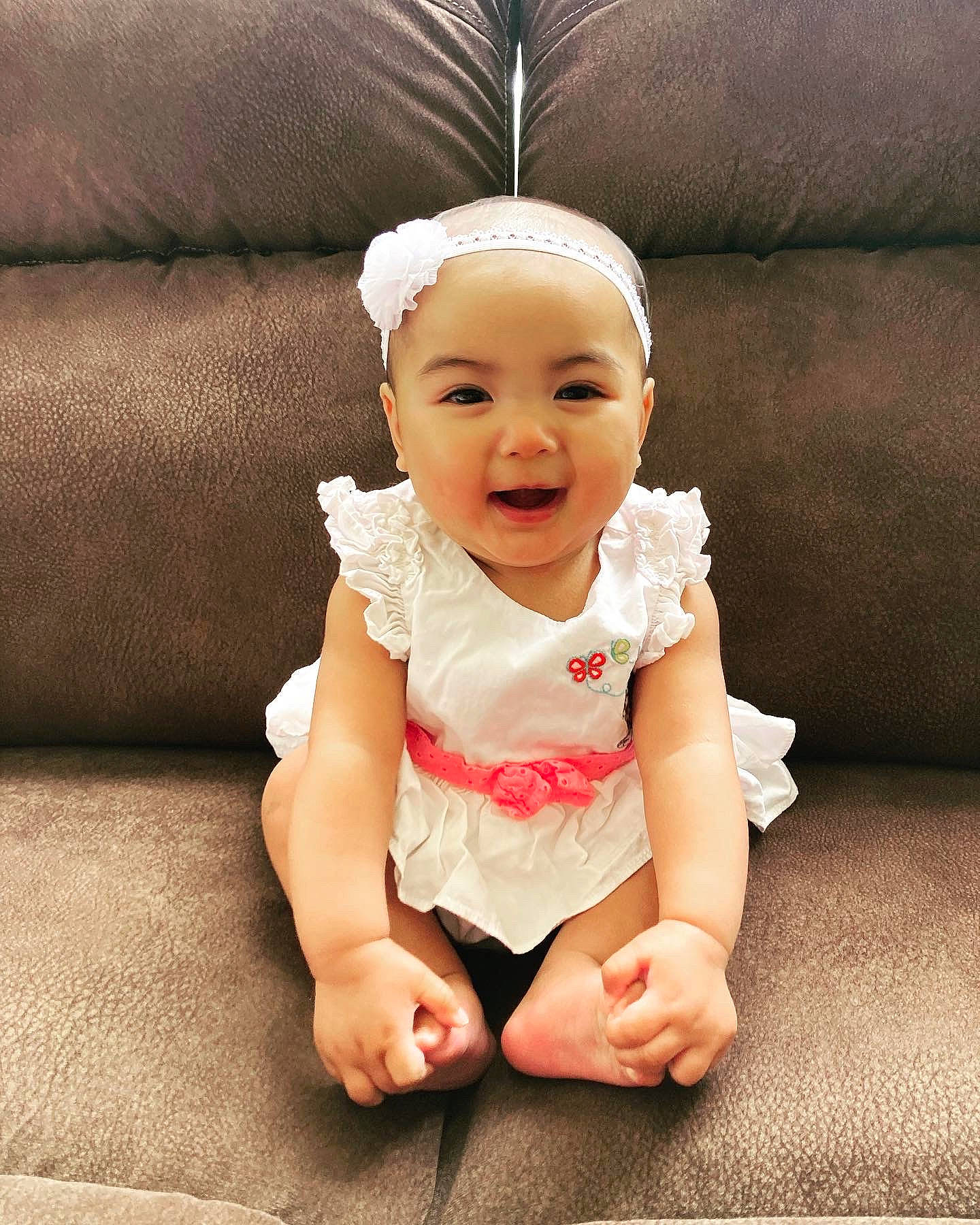 Lexie is registered to the contest to win money with this photo: arm, baby, baby_toddler_clothing, cap, cheek, comfort, costume_hat, couch, eye, fashion_accessory, flooring, foot, happy, human_body, leg, person, sitting, sleeve, smile, thumb