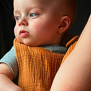 Messer joined the competition — help win amazing prizes! baby, child, face, blue_eyes, orange_cloth, arm, skin, person, portrait, holding, closeup, expression, indoor, soft_light, gentle, candid, human, infant, looking_away, parent